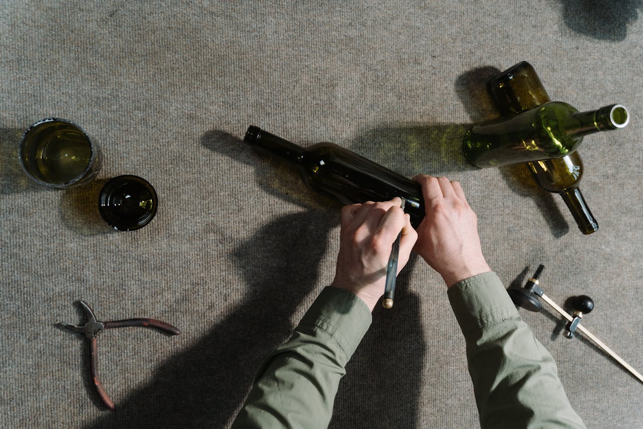 Top view of hands using tools to cut glass bottles, showcasing craftsmanship.