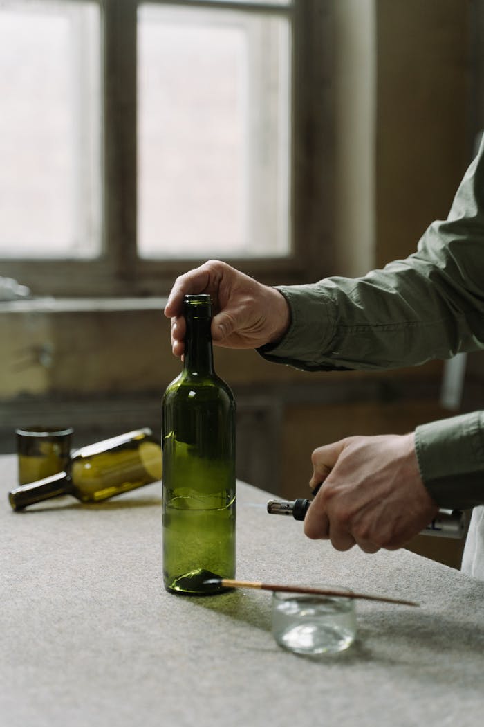 Artisan transforming a wine bottle with a blow torch in an indoor workshop.