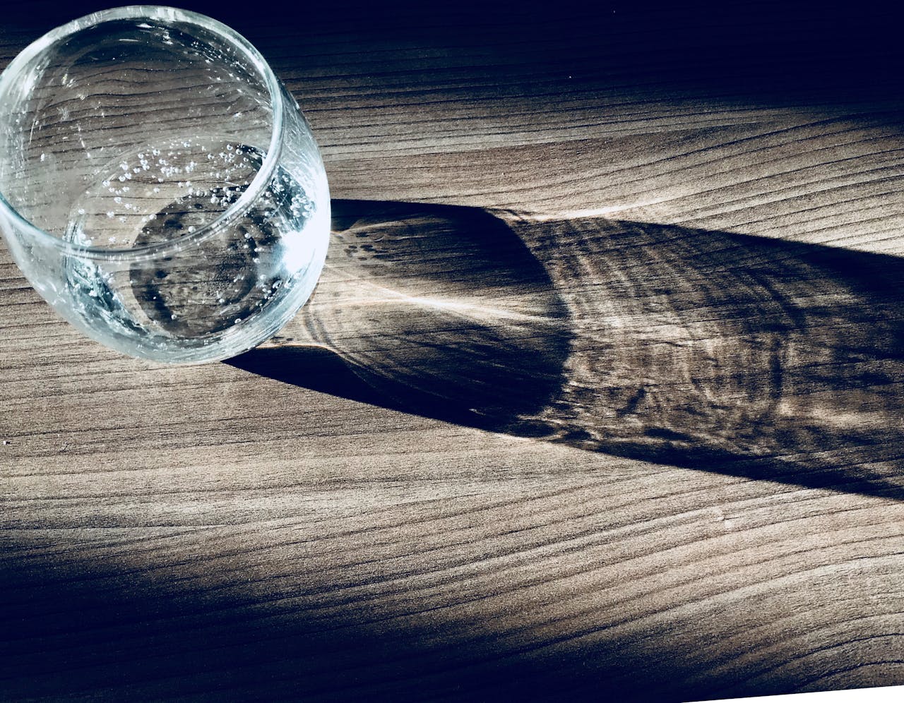 A glass of water casting a shadow on a wooden table, creating an artistic play of light and shadow.